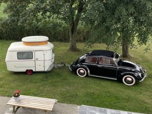 VW Käfer mit Wohnwagen auf einer Wiese